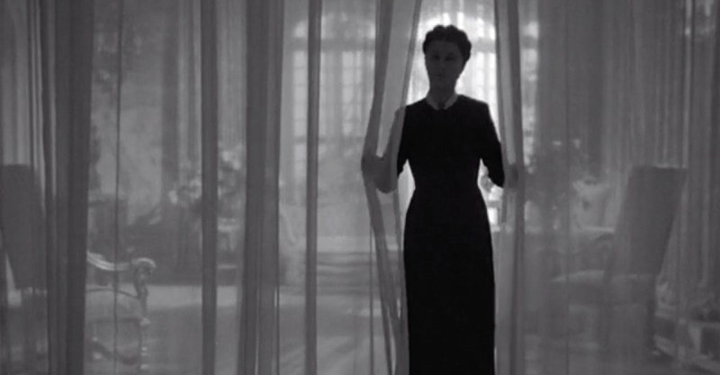 The shadowy figure of Mrs. Danvers appearing through a pair of curtains. 