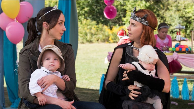 Anne and Kate at a child's birthday party having a serious conversation wearing silly crowns