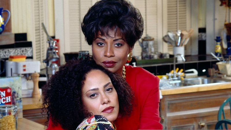 two beautiful queer Black women in 90s power outfits in their kitchen