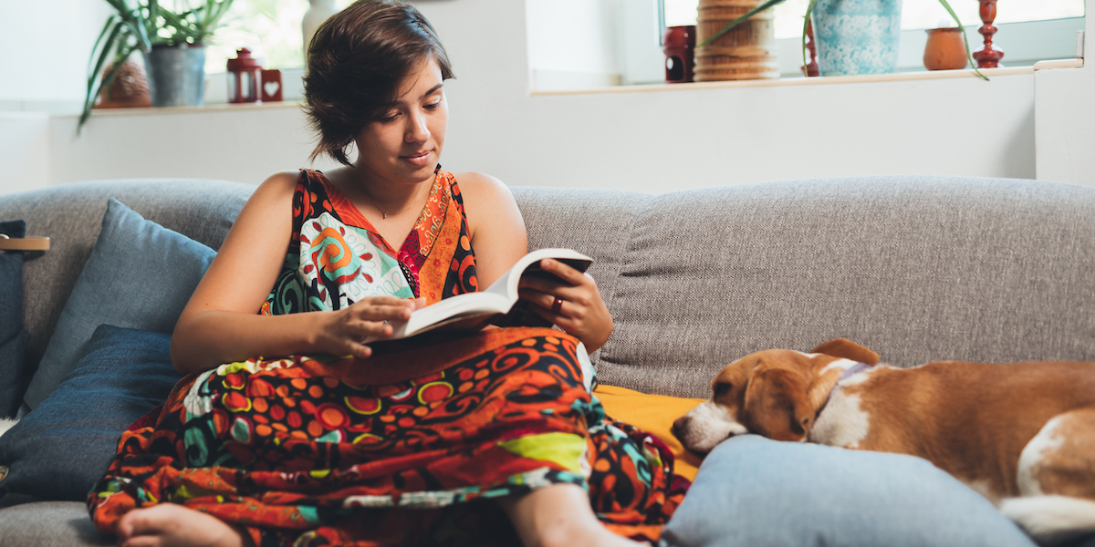 A person reading on a couch in a dress with a dog asleep next to them