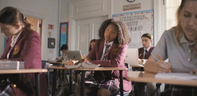 Angelica sits at her desk in her school uniform, bored