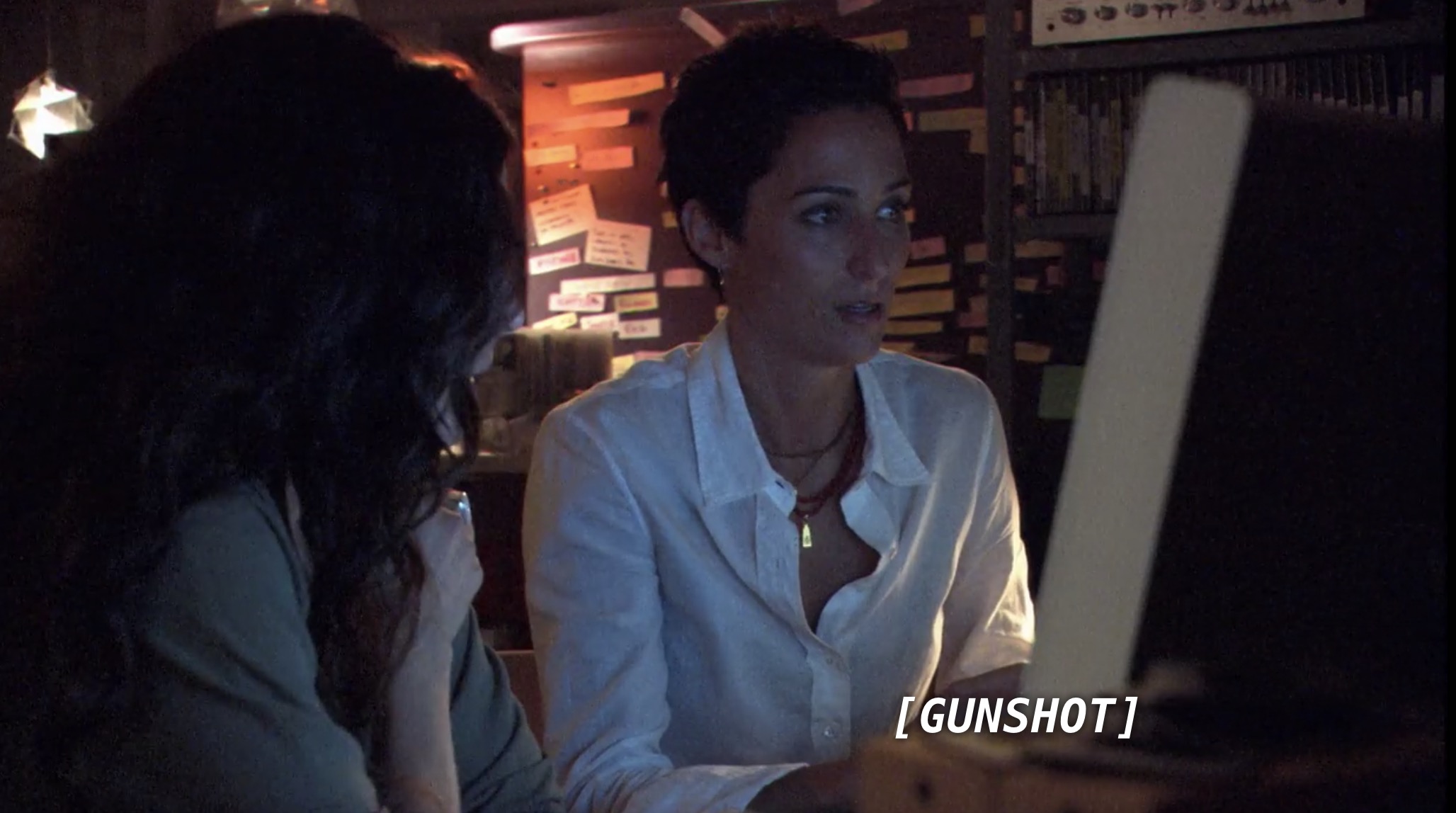 Helena and Dylan sit in front of a computer screen in a dark room. The sound of a gunshot comes from the computer.