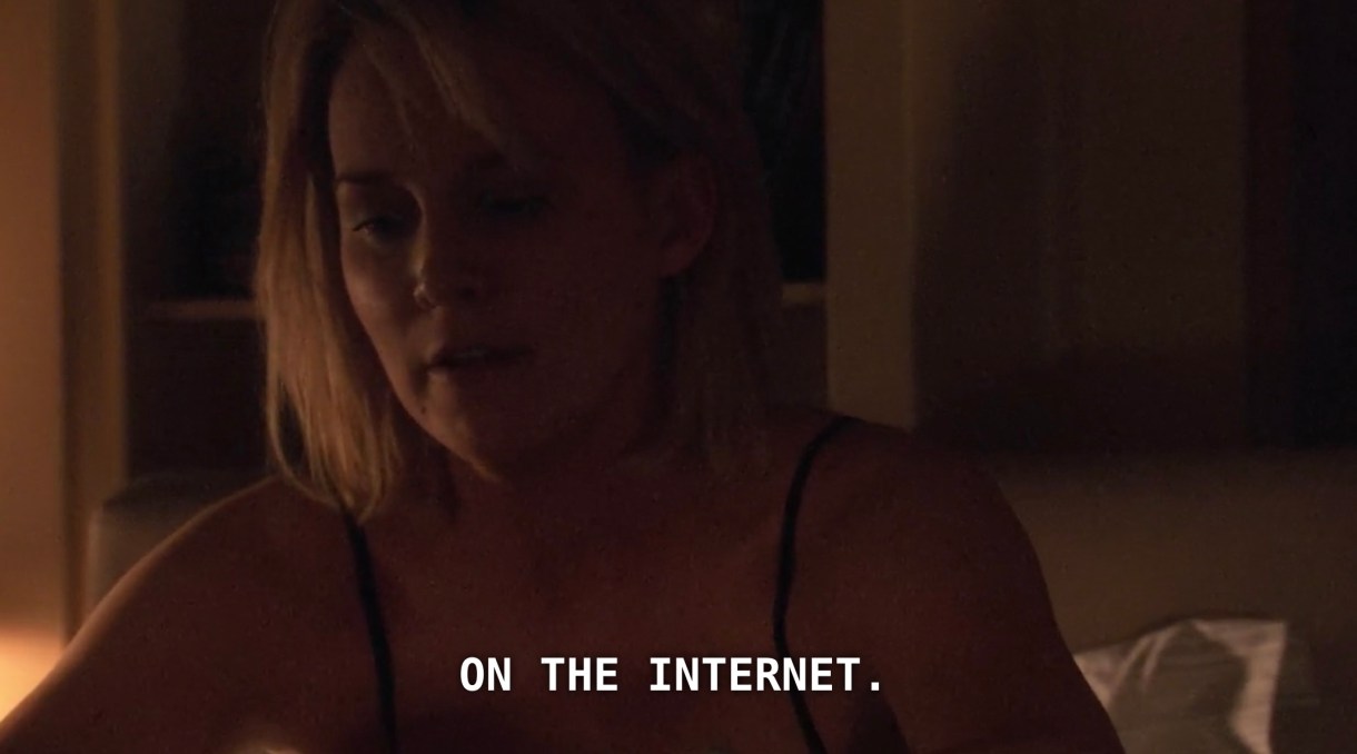 Tina is wearing a black tank top and is a dimly lit bedroom. She says, "on the Internet."