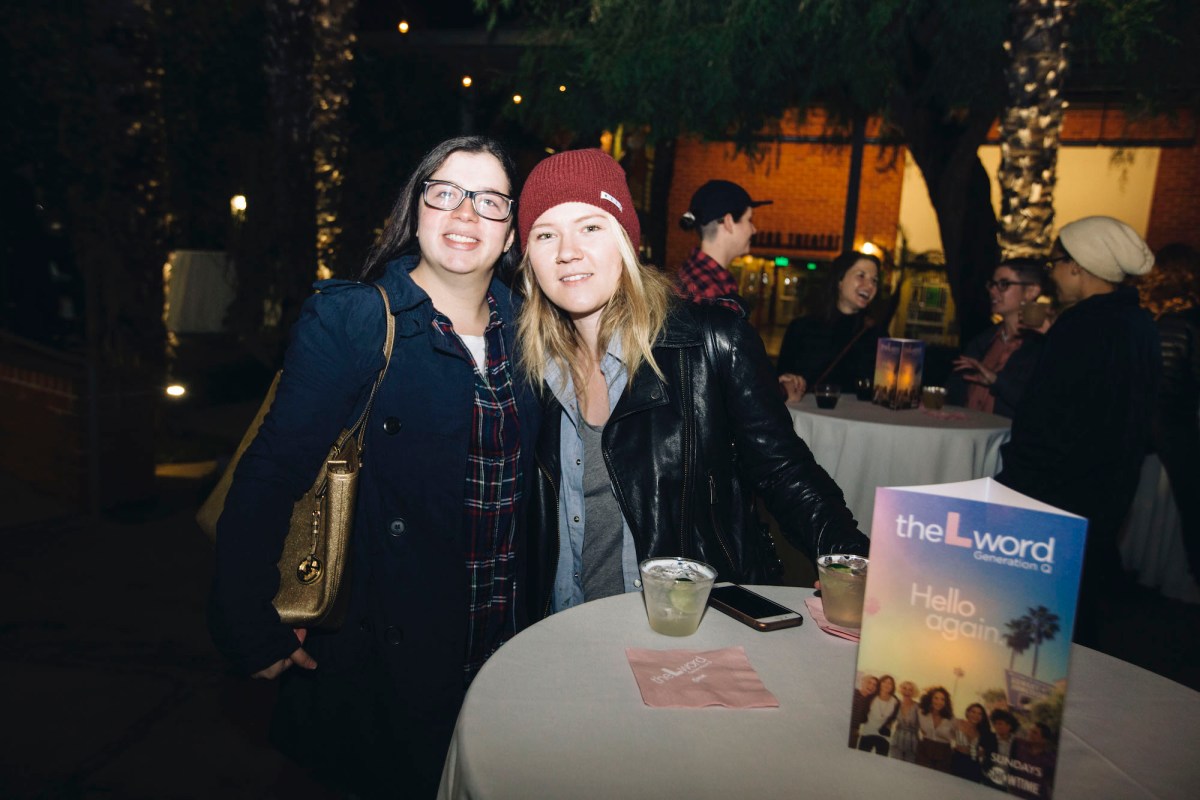 Two people pose for a photo, standing behind a tall circle cocktail table featuring drinks and a table topper advertising "The L Word: Generation Q"