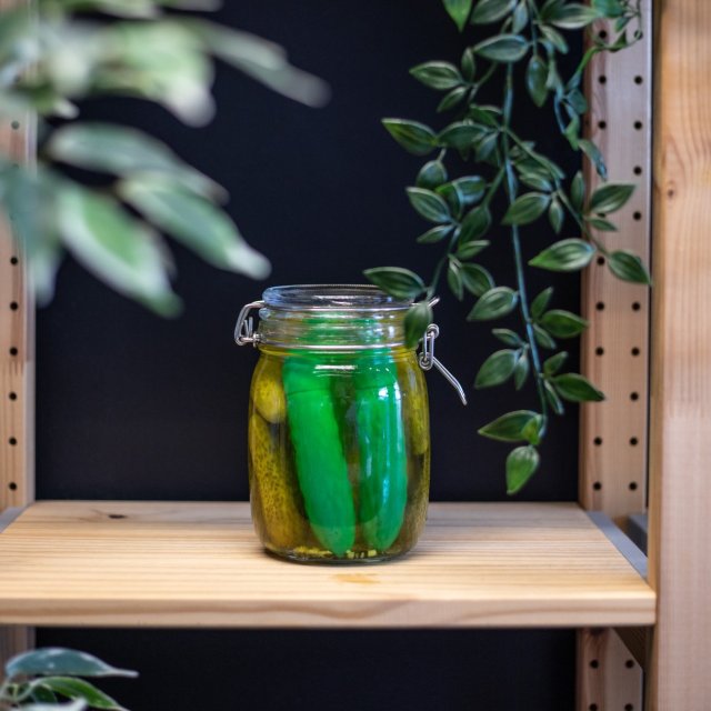 a pickle-shaped vibrator in a jar of actual pickles on.a shelf