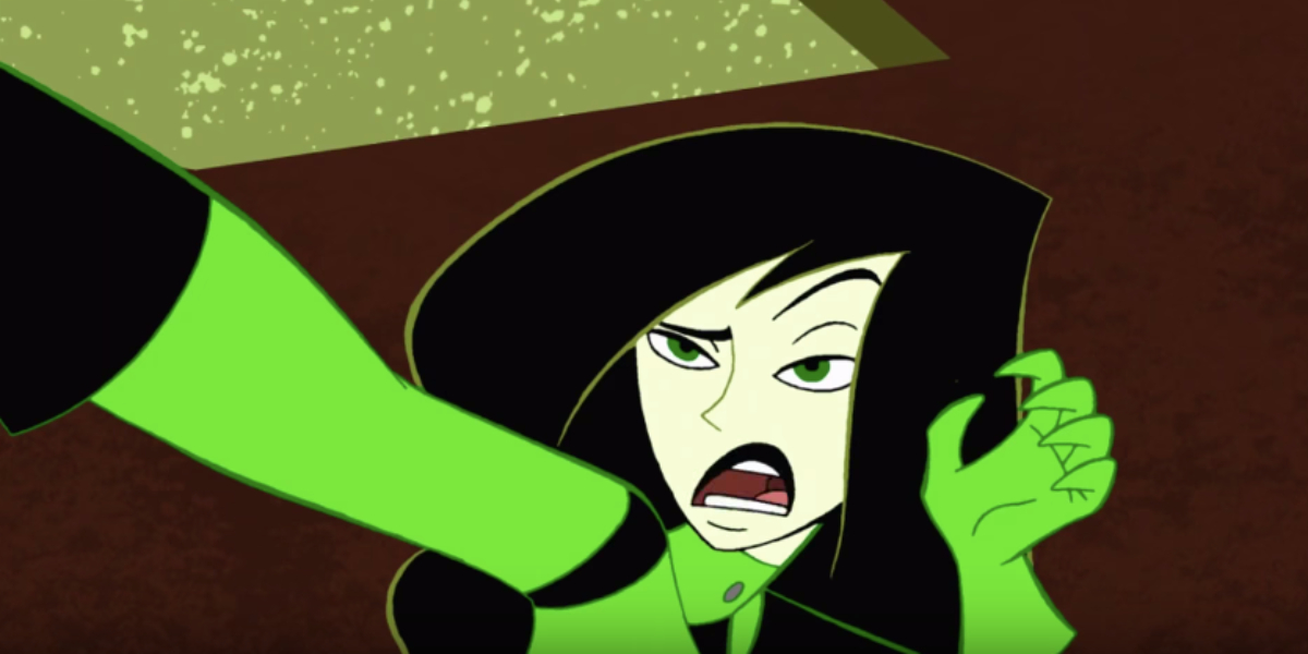 Shego, a young woman from Kim Possible, has Black hair, pale skin, and green eyes. She is pinning someone to a wall with one hand, and holding her other hand up toward her face.