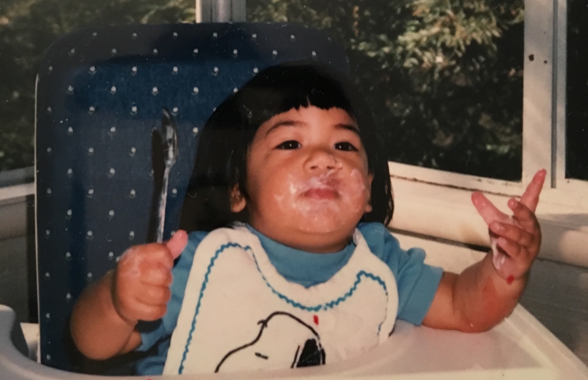 chubby faced toddler sits in high chair with yogurt smeared on her cheeks