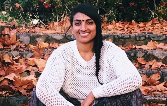 person smiling in white knit sweater with braid and black bindi