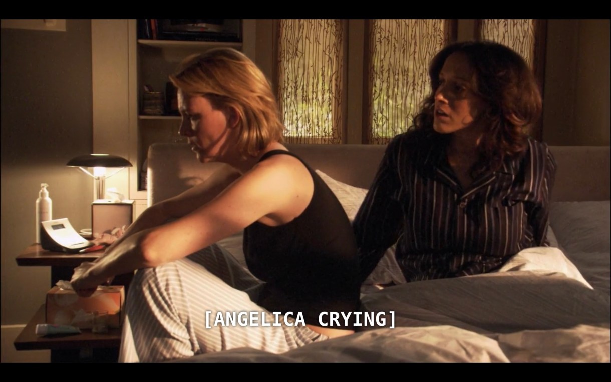 Tina (wearing striped pajama bottoms and a black tank top) sits next to Bette (wearing a black pinstripe PJ set) in their bed. The subtitles read "Angelica crying" off camera.