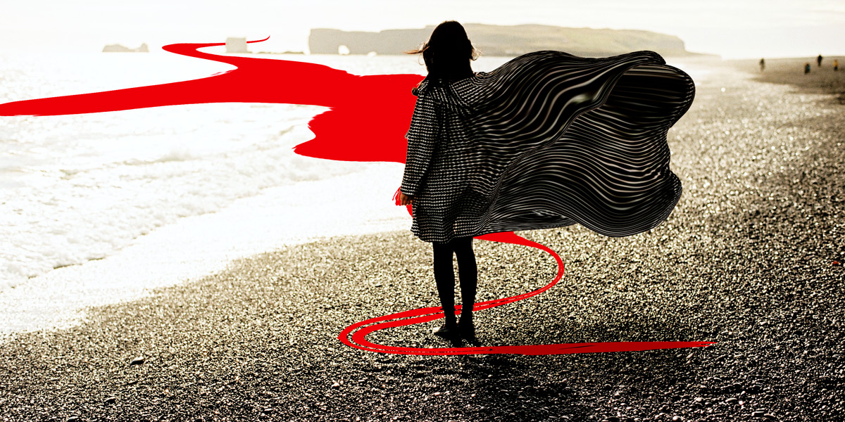 woman standing at edge of water with cape flying and a swirl of red around her