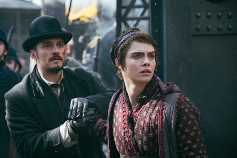 Image: A man in a hat with facial hair stands next to Cara Delevingne, who has short hair like an elf and a headband