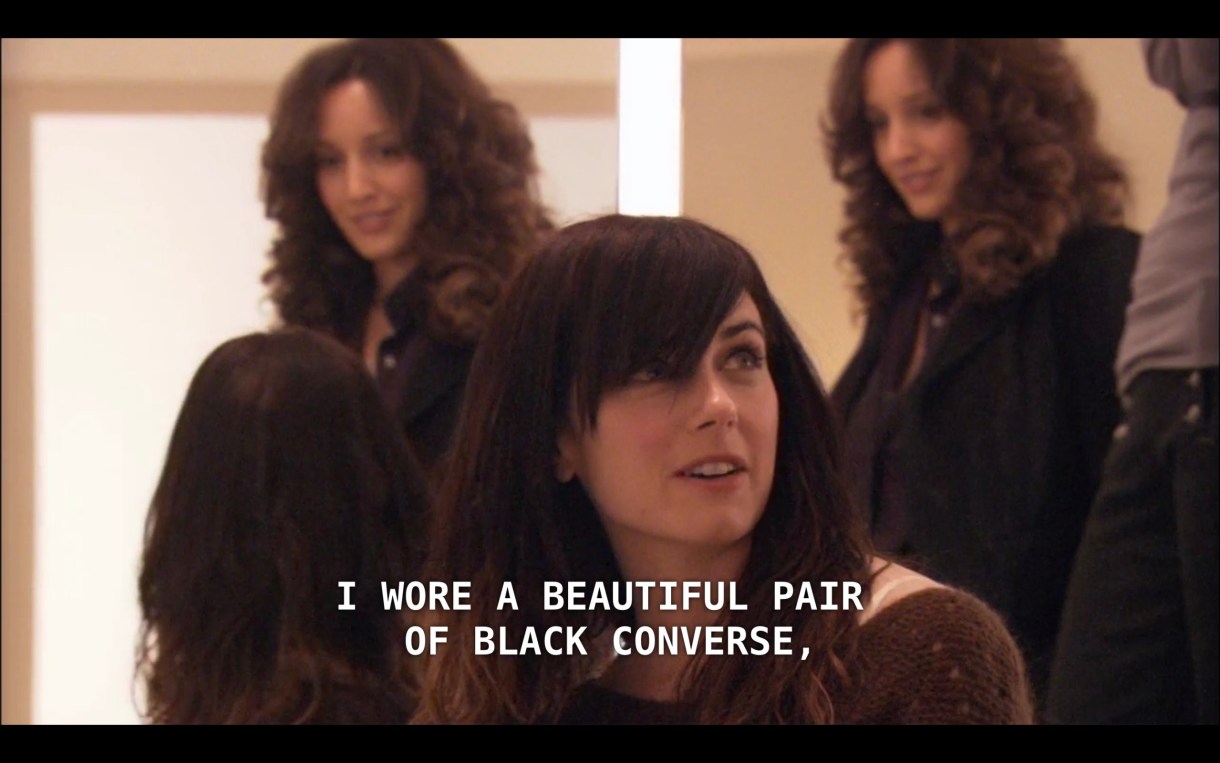 Jenny (wearing a brown sweater and iconic side swoop bangs) sits in the bridal store. Bette is standing behind her in a black jacket. Jenny is talking about when she got married, saying, "I wore a beautiful pair of black converse."