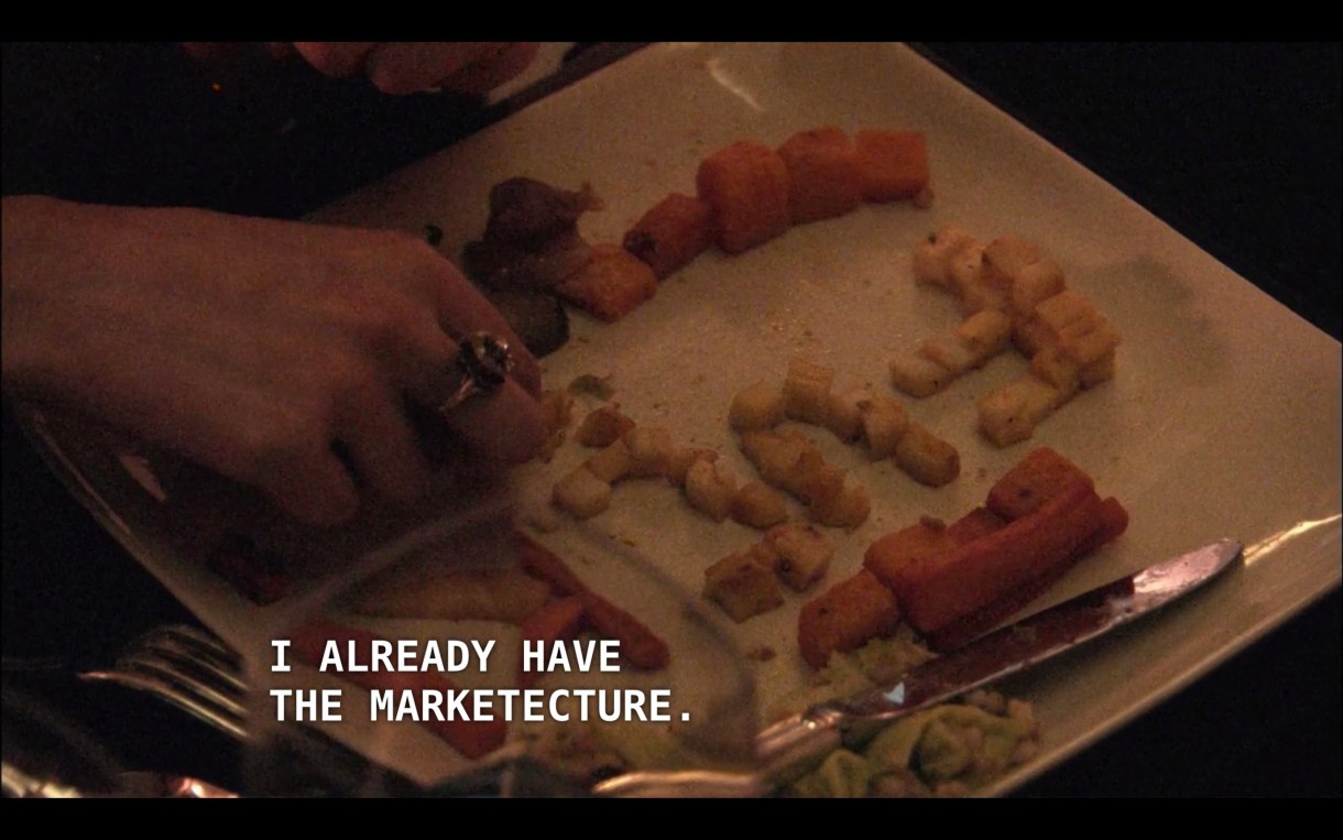 A white square dinner plate featuring tiny carrots and potatoes. Just in frame, Jenny's hand is spelling out "FUC" in tiny potatoes. Off screen, Max's boss's wife says, "I already have the marketecture."