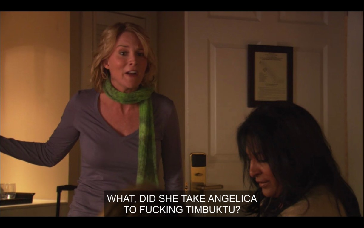Tina, wearing a green scarf and a purple v-neck, has barged into the hotel room and is asking her friends if Bette took Angelica to Timbuktu