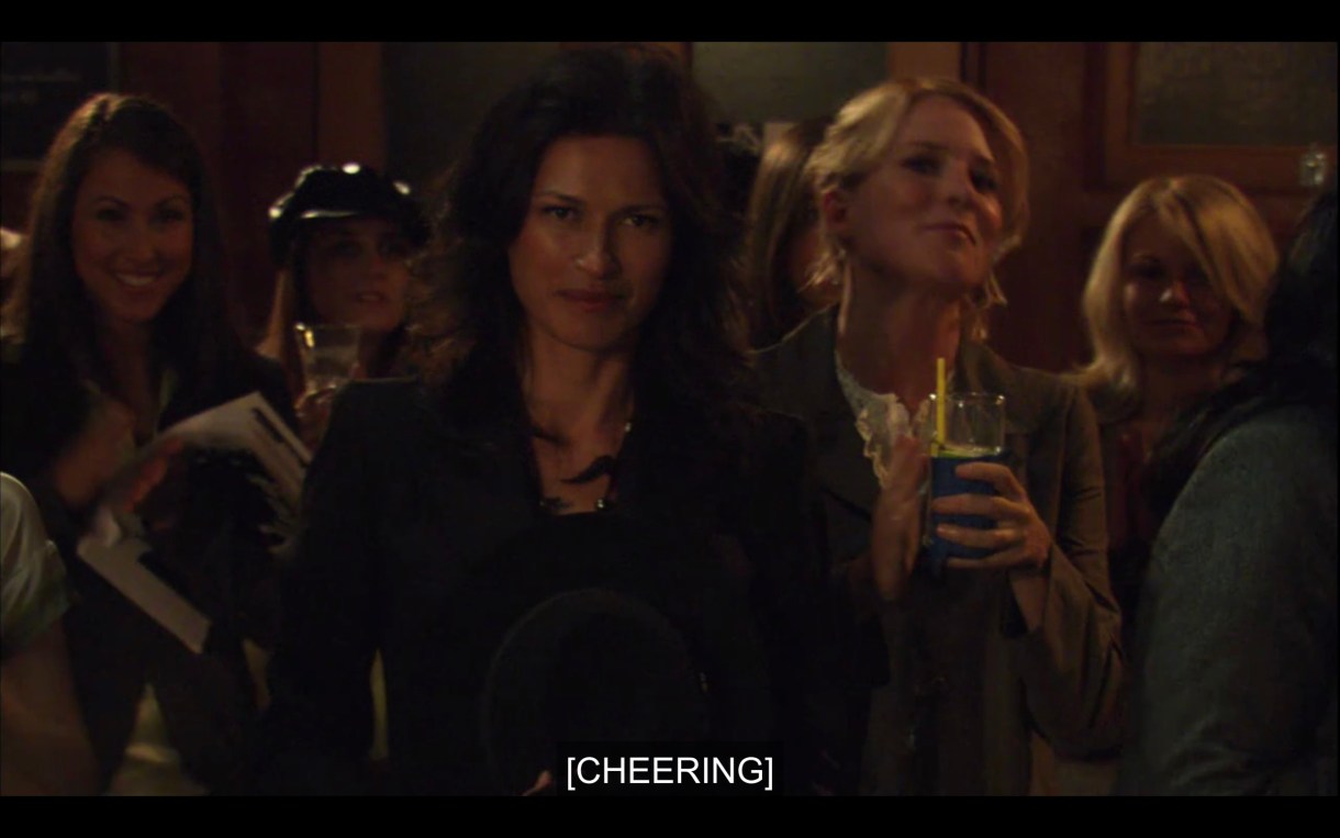 Marina shows up at Jenny's reading. Tina is standing behind her holding a drink. Subtitles read, "[Cheering]"