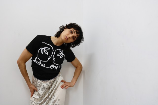 Model wears Official Rebrand black t shirt against a white wall.
