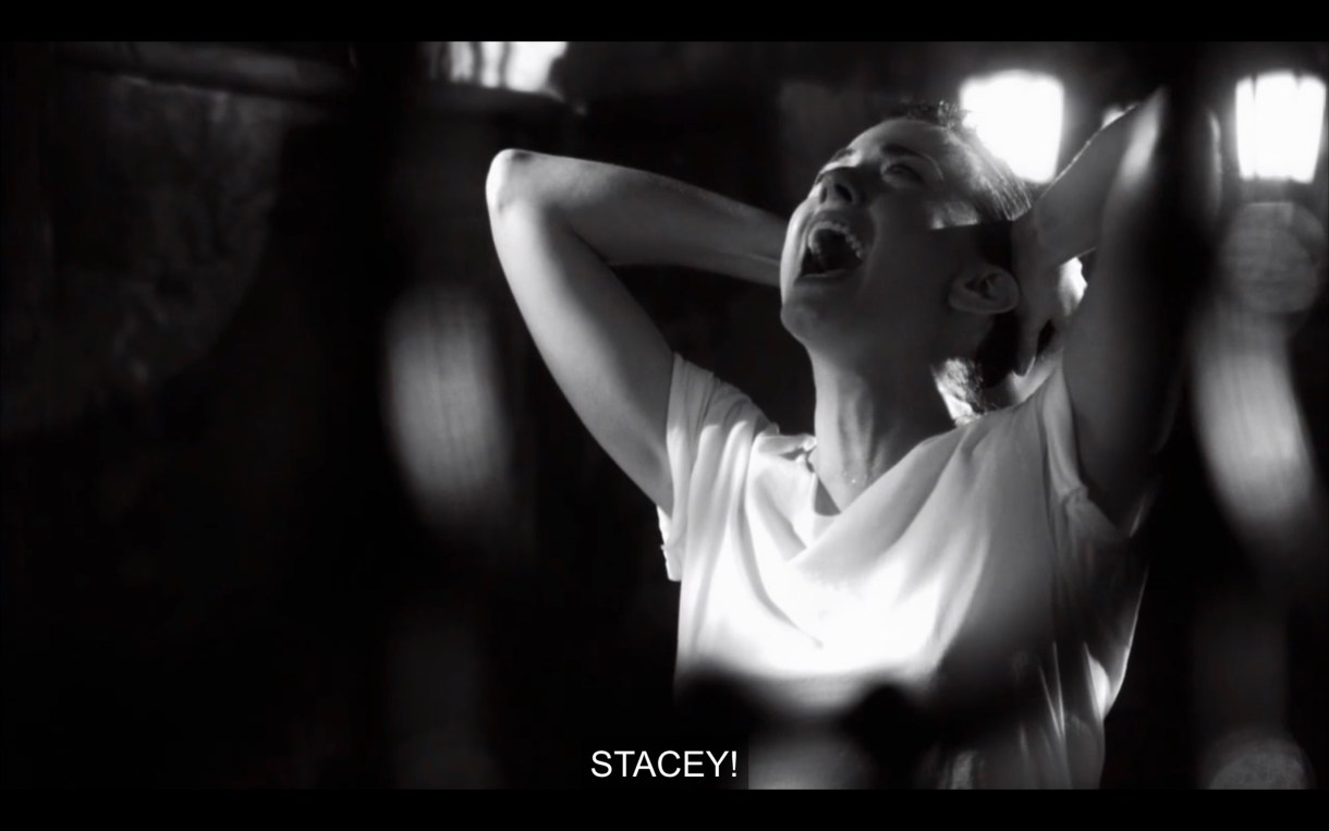 Black and white shot. Jenny in a white t-shirt with her hands behind her head. She yells, "Stacey!"