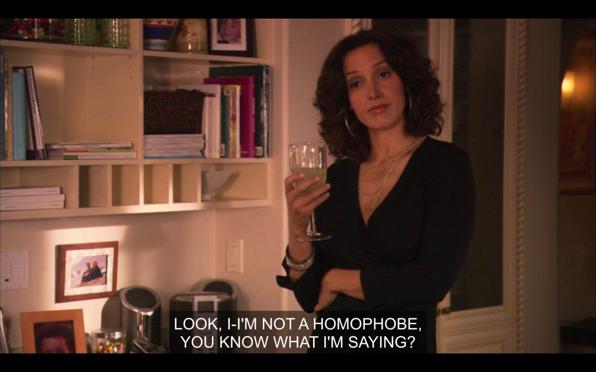 Bette stands with a wine glass in her hand as a straight cis partygoer, off camera, says, "Look, I-I'm not a homophobe, you know what I'm saying?" She has a "what in the actual fuck?" look on her face.