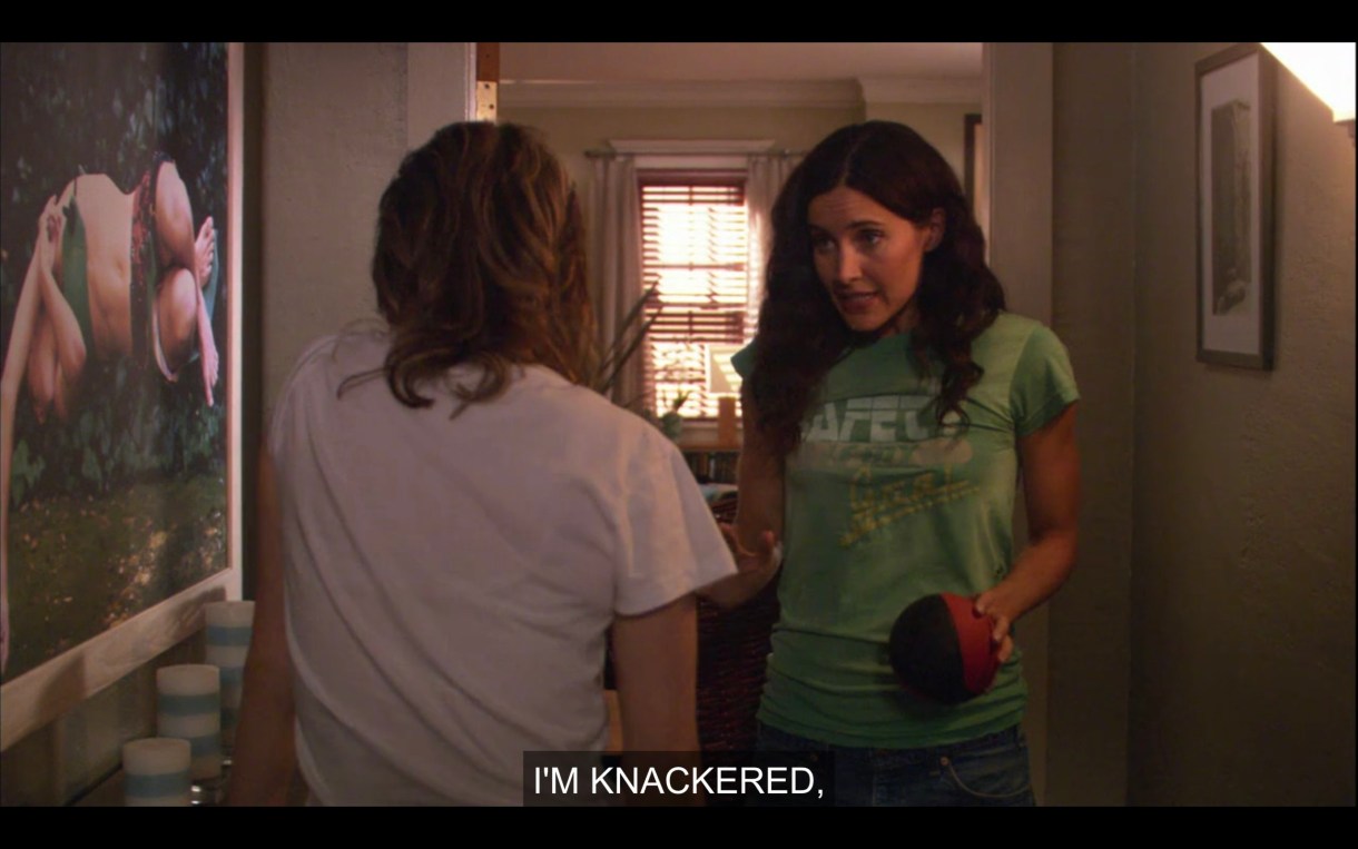 Helena and Alice in their apartment hallway. Alice is in a white t-shirt and her back is to the camera. Helena is in a green t-shirt and holding a small basketball. Helena says, "I'm knackered."