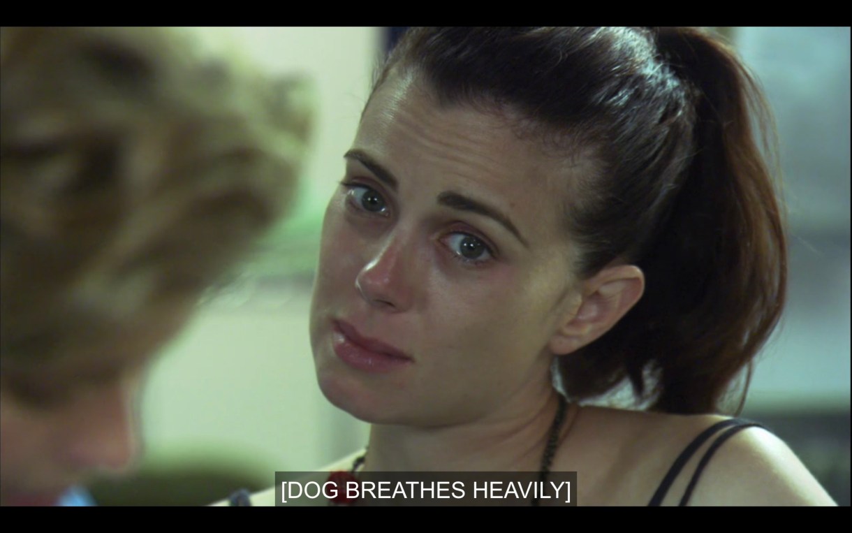 Close-up of Jenny with tears in her eyes. She's wearing a black tank top and her hair in a ponytail. Subtitles read, "[Dog breathes heavily]"