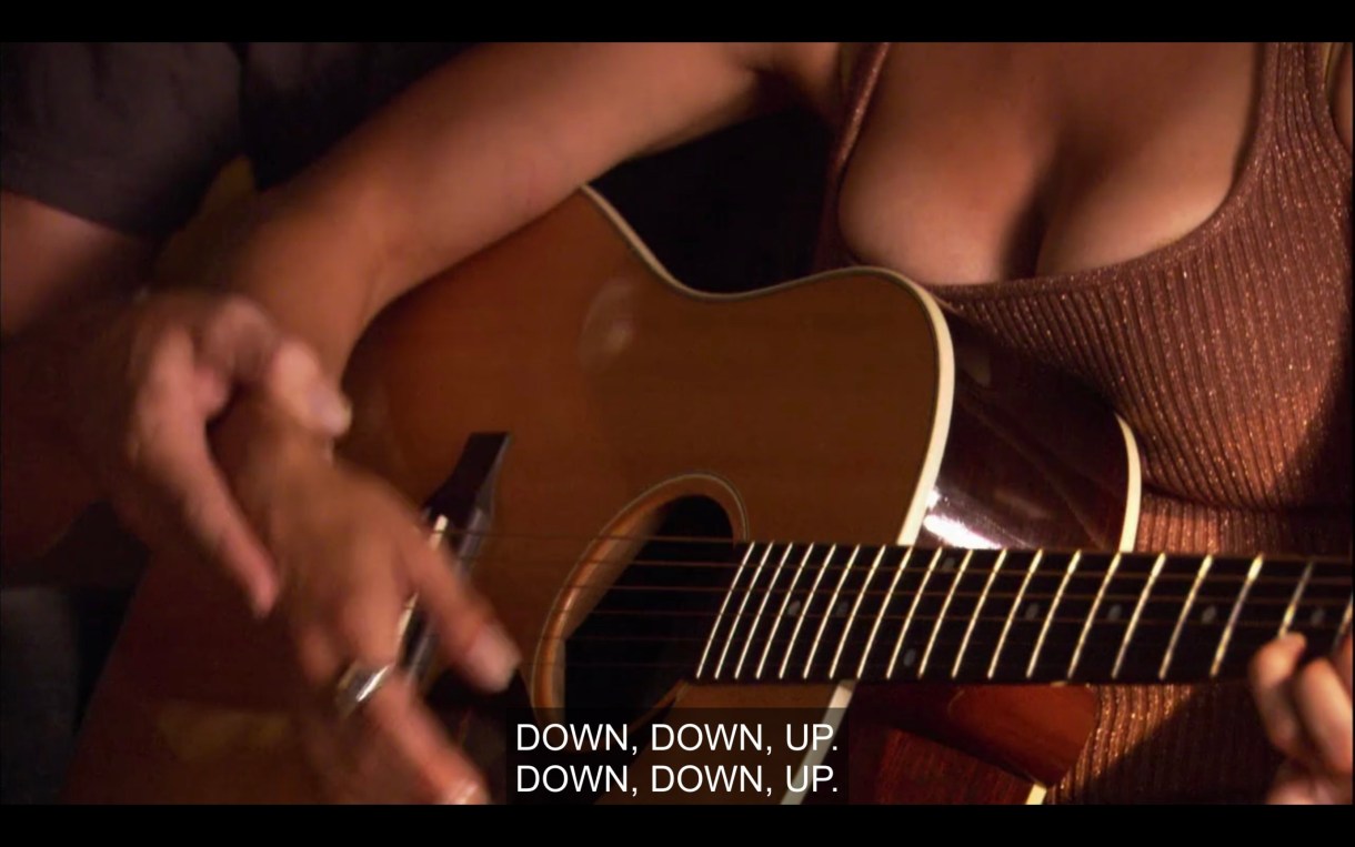 Close-up shot of hands playing a guitar. "Down, down, up. Down, down, up."