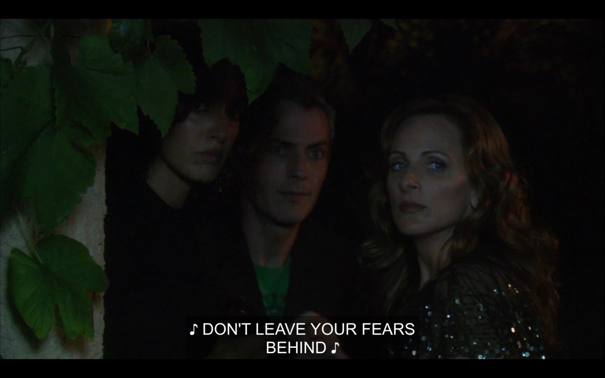 Bette, Tom, and Jodi stand together outside in the dark. Music is playing, singing, "Don't leave your fears behind."