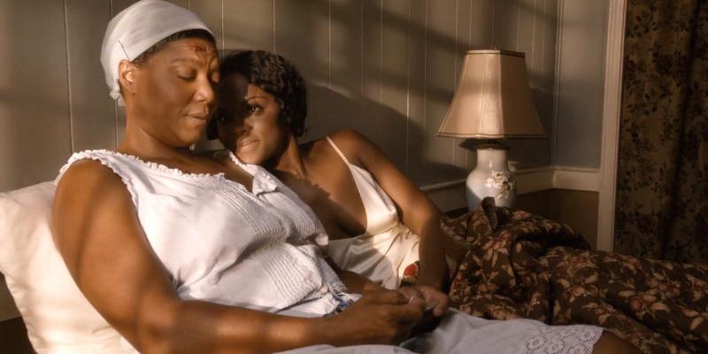 A still from Bessie. Queen Latifah wearing white in bed with another woman.