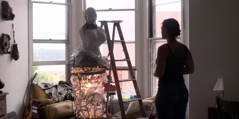 A woman looks at a multimedia sculpture she's making.
