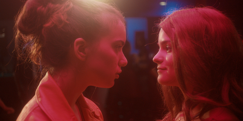 Two girls look at each other in red lighting.