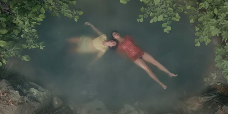 Two girls lie on their bakes in a small pond.