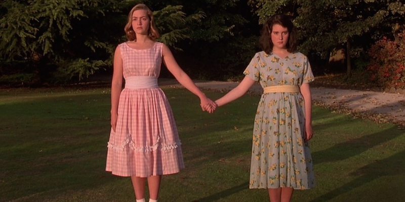 Kate Winslet and Melanie Lynskey in pastel dresses hold hands.