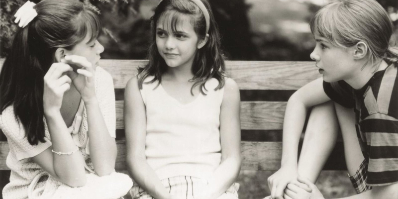 Three young girls sit on a bench together. 