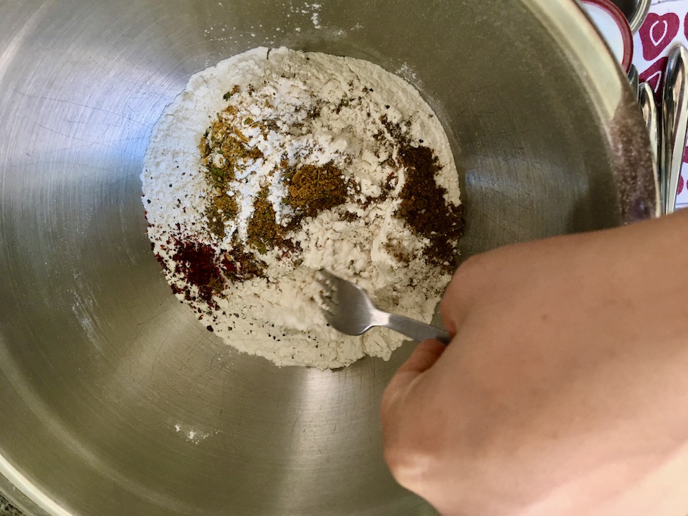 silver mixing bowl with colored spice piles on top of flour