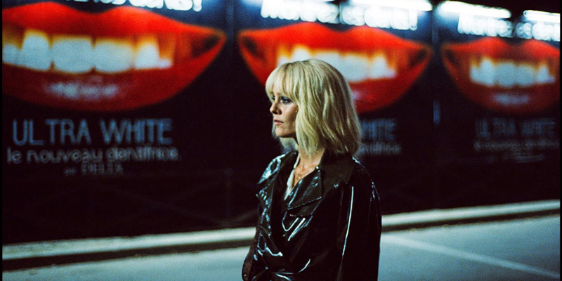 A woman with a black vinyl jacket stands in front of an ad for teeth whitening.