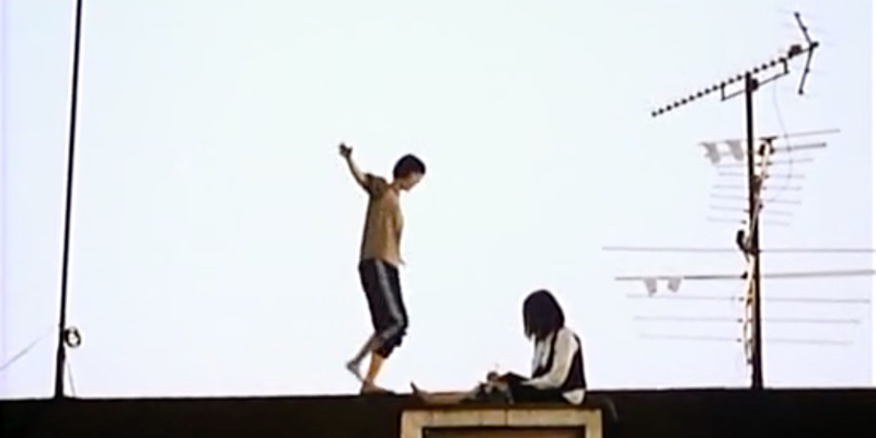 A girl walks along the roof of a school next to another girl who is seated.