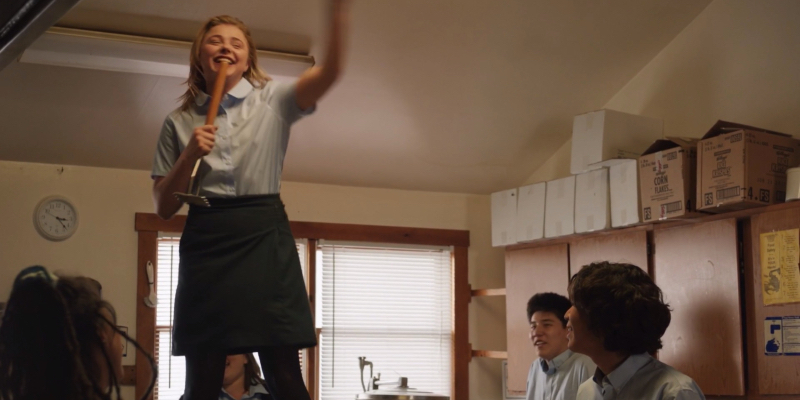 A still from The Miseducation of Cameron Post. Chloe Grace-Moretz stands on a counter singing into a makeshift microphone.