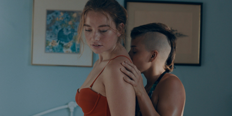 A nonbinary person kisses the back of a girl in a red bikini.
