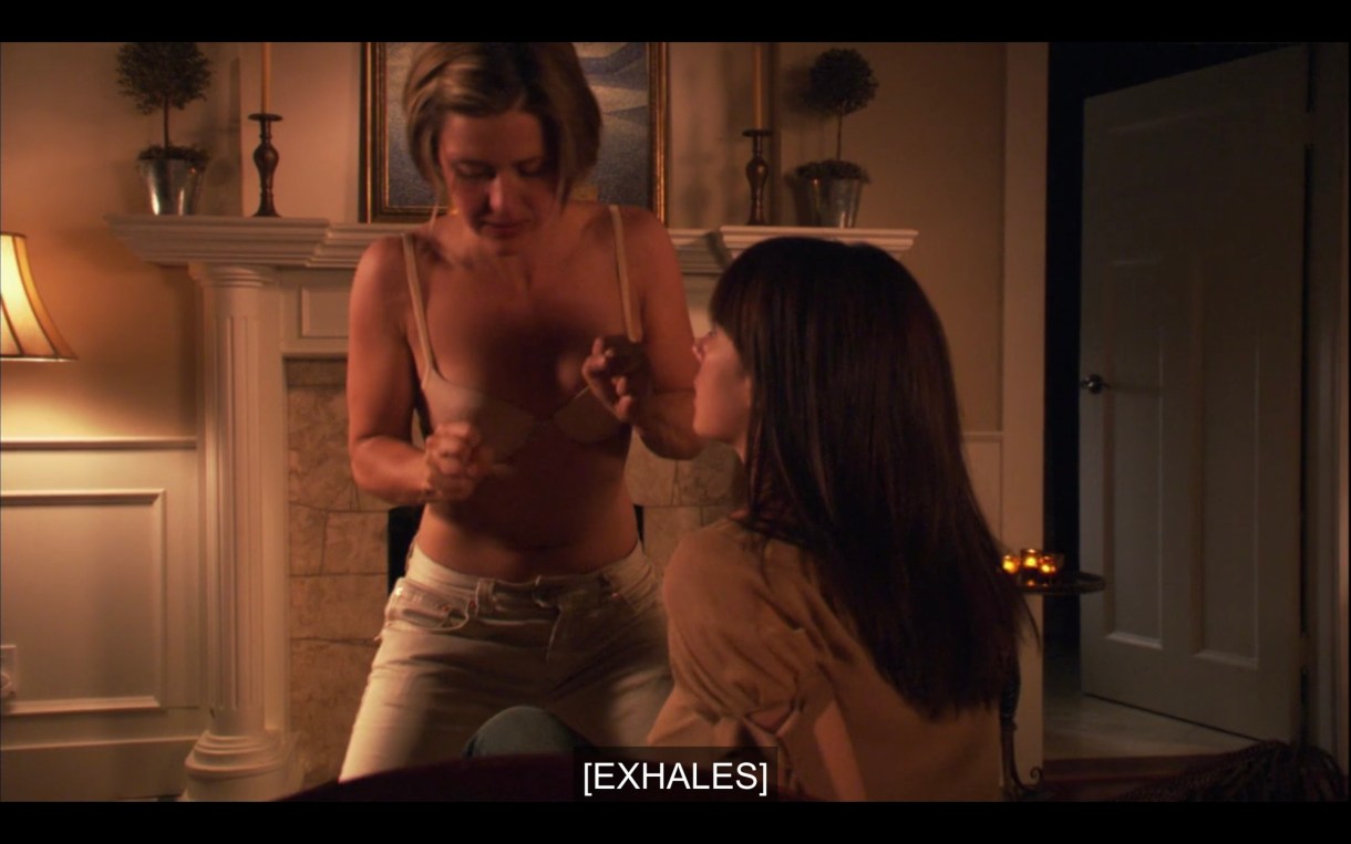 Lindsey (wearing her bra and pants) straddles Jenny, who is sitting up on the couch. Subtitles read, "[Exhales]"