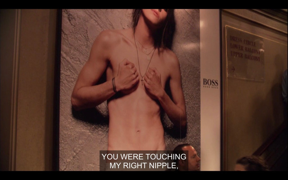 Shane's billboard. In the photo, she is standing in front of a concrete wall, topless, with her hands covering both of her boobs. She's wearing a cross necklace and her head is tilted to the side. Off camera, someone says, "You were touching my right nipple."