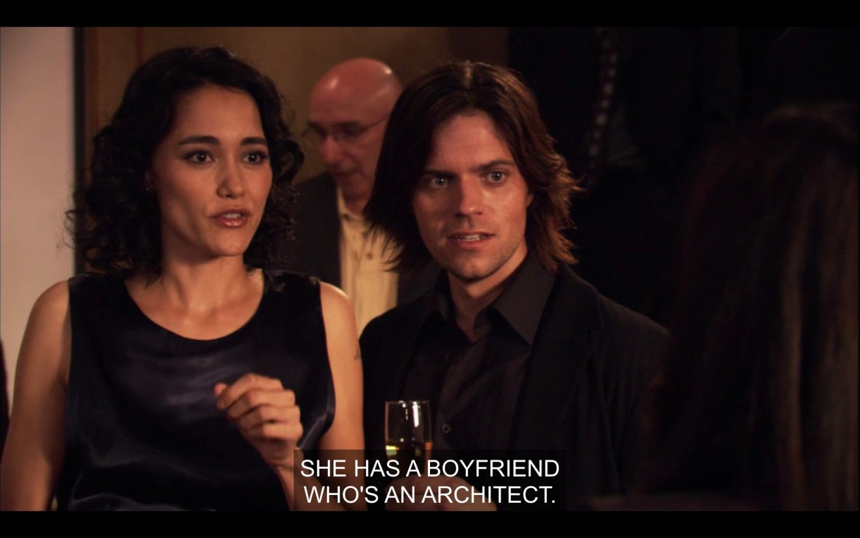 A dark-haired man (wearing a suit and tie and holding a glass of wine) and dark-haired woman (wearing a black dress) look shocked and confused. "She has a boyfriend who's an architect."