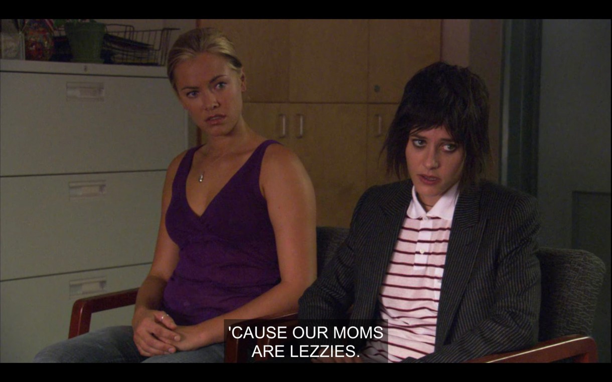 In the principal's office. Paige wearing a purple tank top and Shane in a polo and a blazer, both looking displeased and shocked. Caption is what one of the off-screen boys is saying, "Cause our Moms are Lezzies."