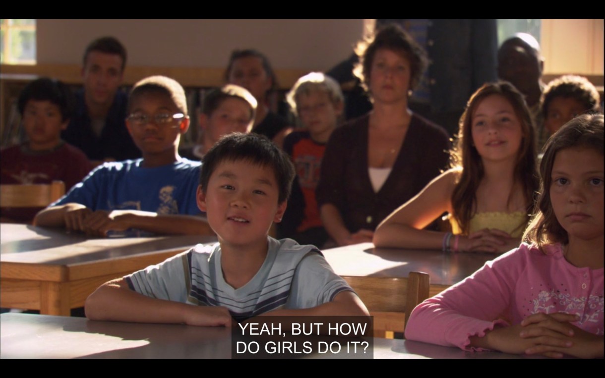 A classroom of children and their terrible parents watching a presentation. A little boy in a striped t-shirt in the front asks, "Yeah, but how do girls do it?"