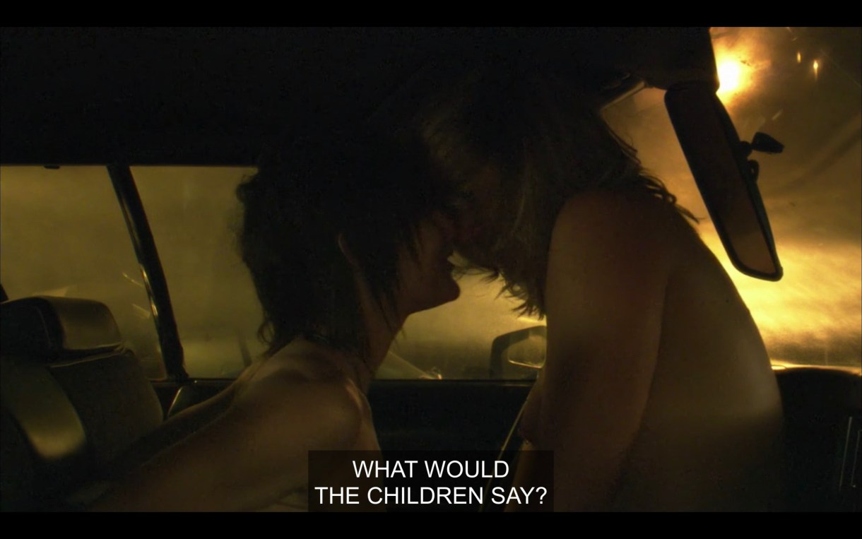 Paige and Shane, both topless, having sex in the car. Paige is straddling Shane and they are kissing. The windows look foggy and it's dark outside. Paige says, "What would the children say?"