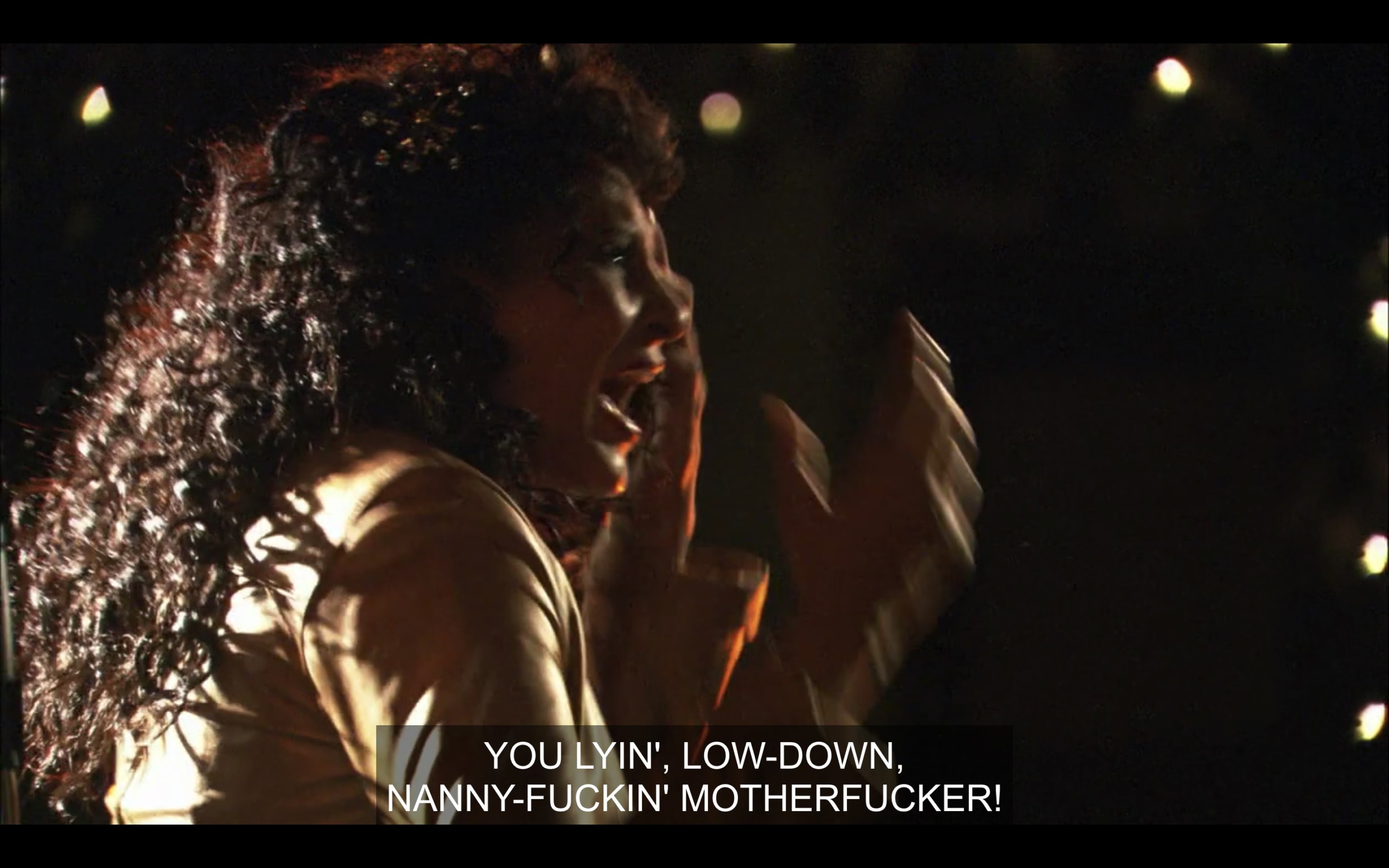 Side-profile shot of Kit, with her arms raised, as she yells, "You lying, low-down, nanny-fuckin' motherfucker!"