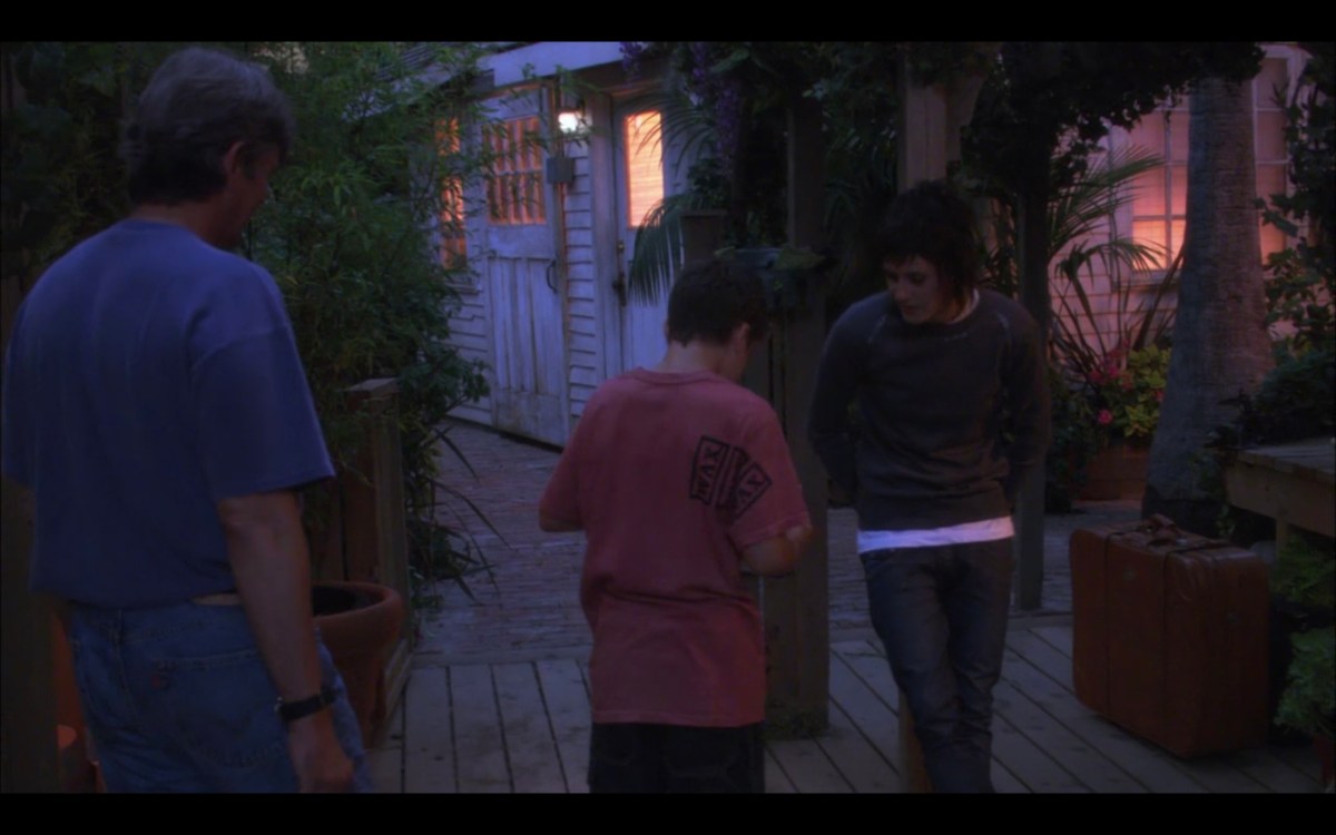 Shane, Shay, and their dad outside at dusk. Shane is leaning against a post. Shay and their dad's backs are to the camera.