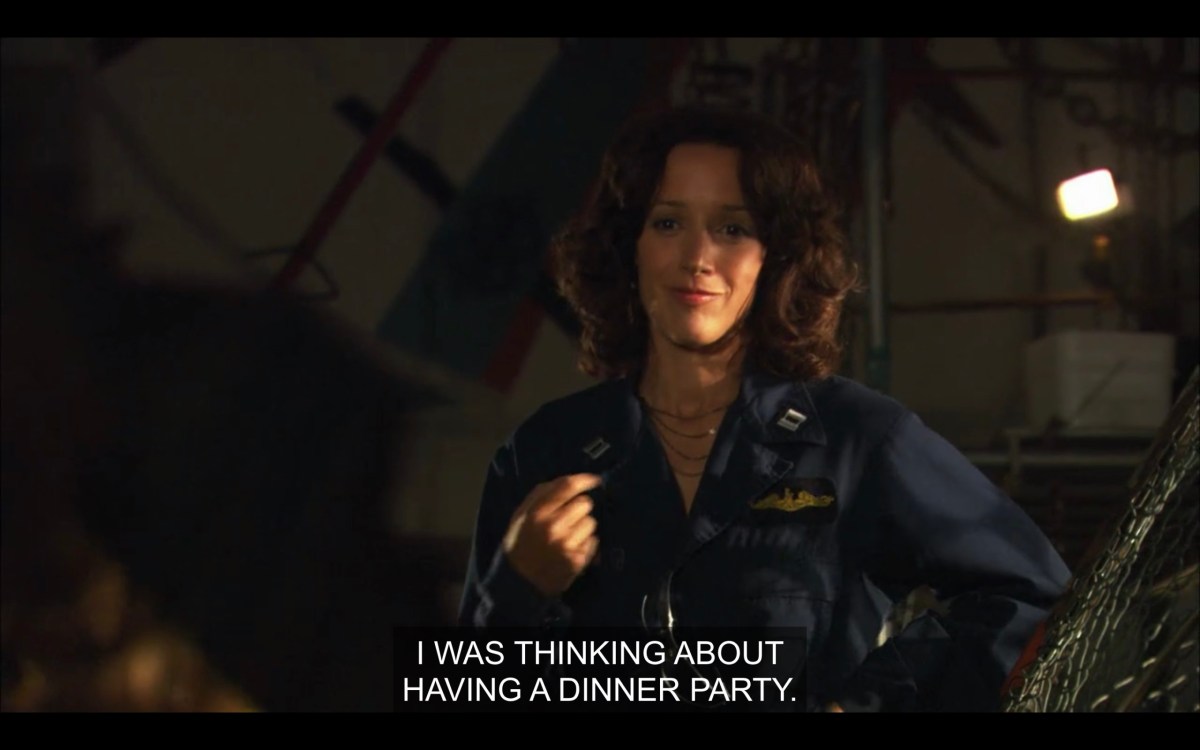 Bette in a blue coverall work suit. She says, "I was thinking about having a dinner party."