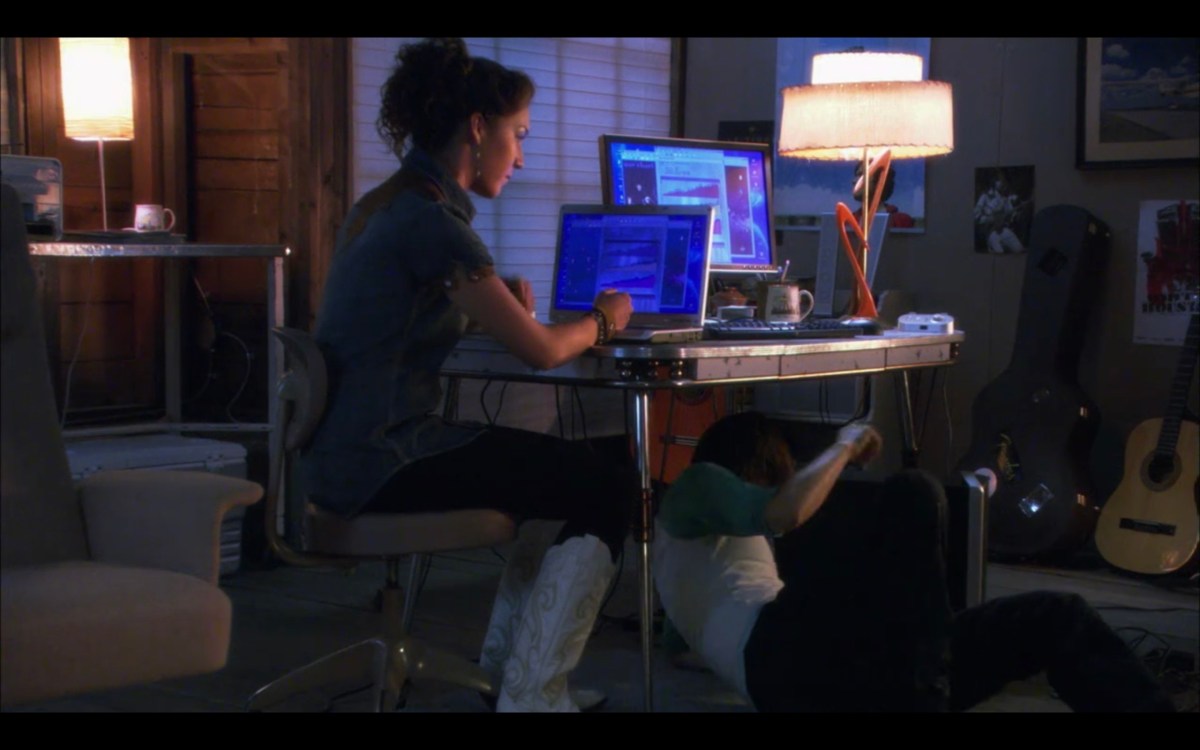 Grace sitting at a desk looking at a blue screen on a laptop. She is wearing very large white cowboy boots.