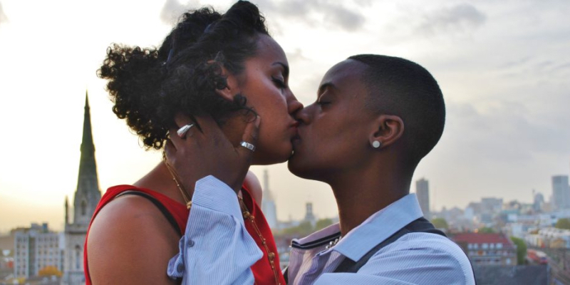 A stud kisses a femme with the London cityscape behind them.
