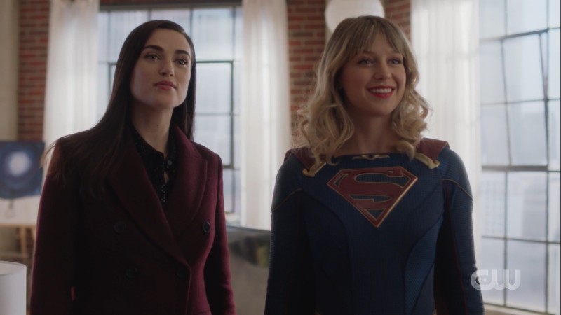 lena stands next to a supergirl smiling