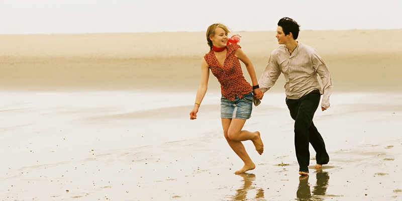 A girl runs on the beach holding hands with a tomboy.